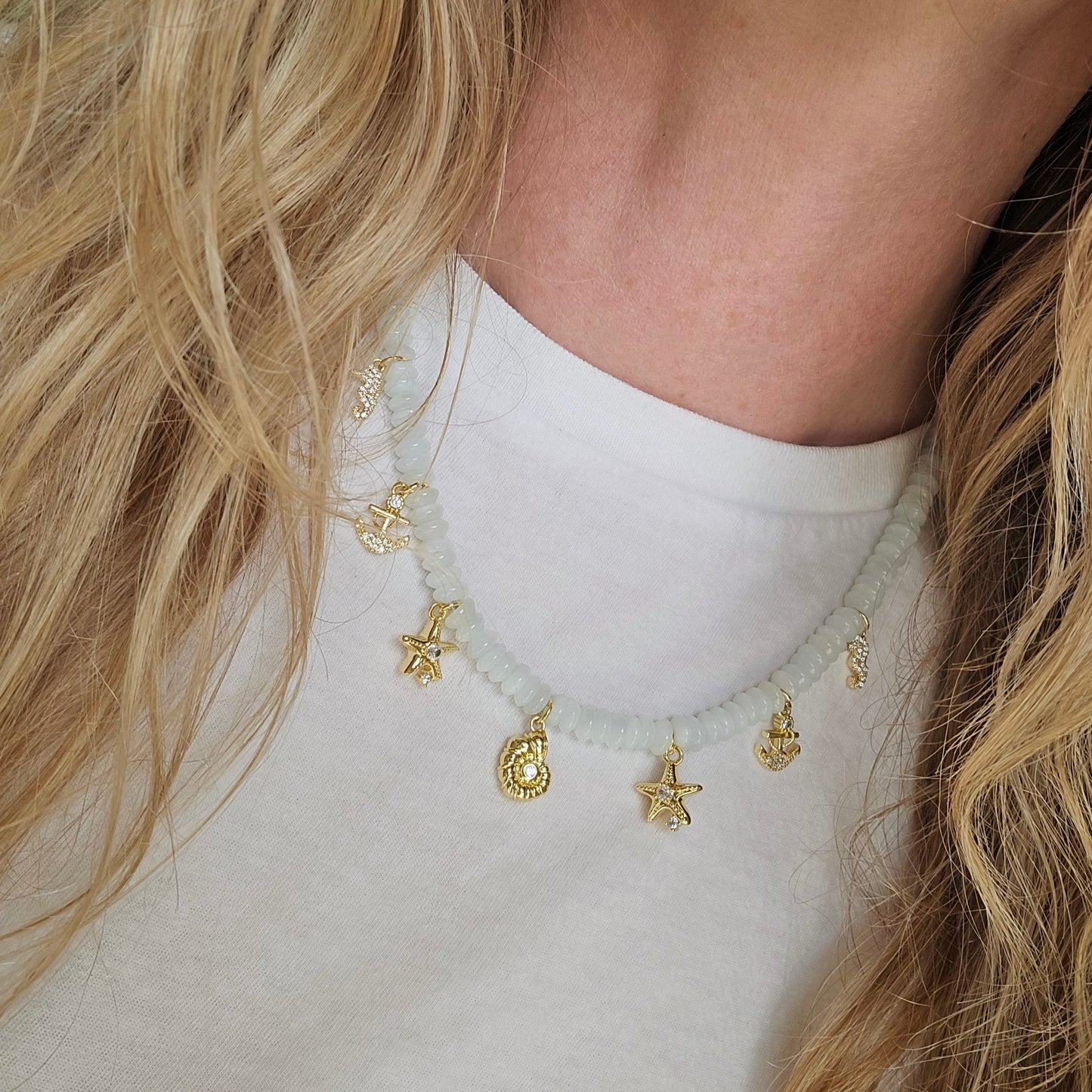 Close-up of a person wearing a delicate gold necklace with small pendants on a plain background