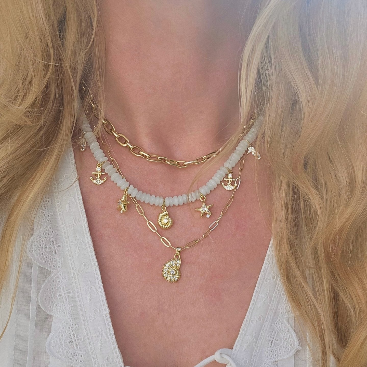 Close-up of a person wearing multiple gold necklaces with various charms against a blurred background.