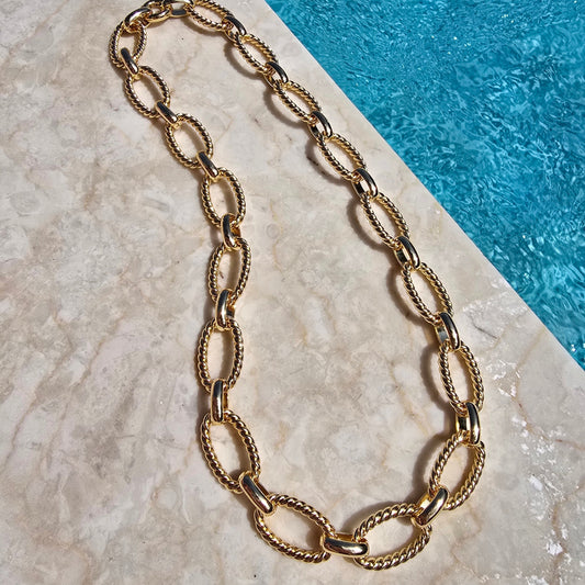 Gold chain necklace on a textured surface with a blue background